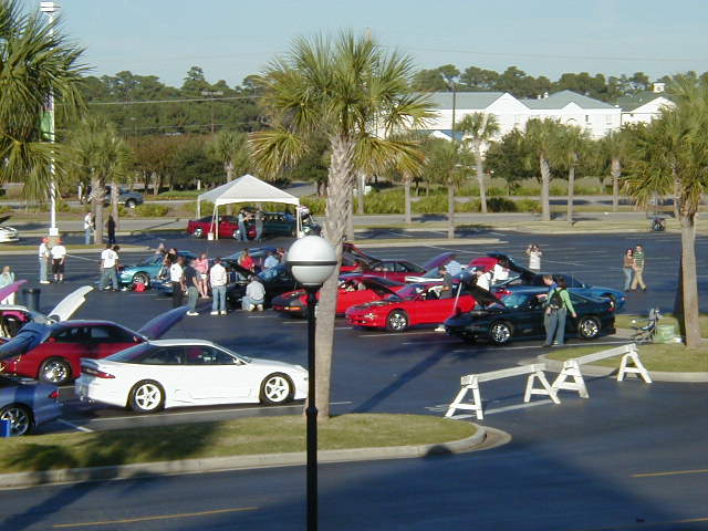 White coupe with hood open, parked in lot with other cars and people