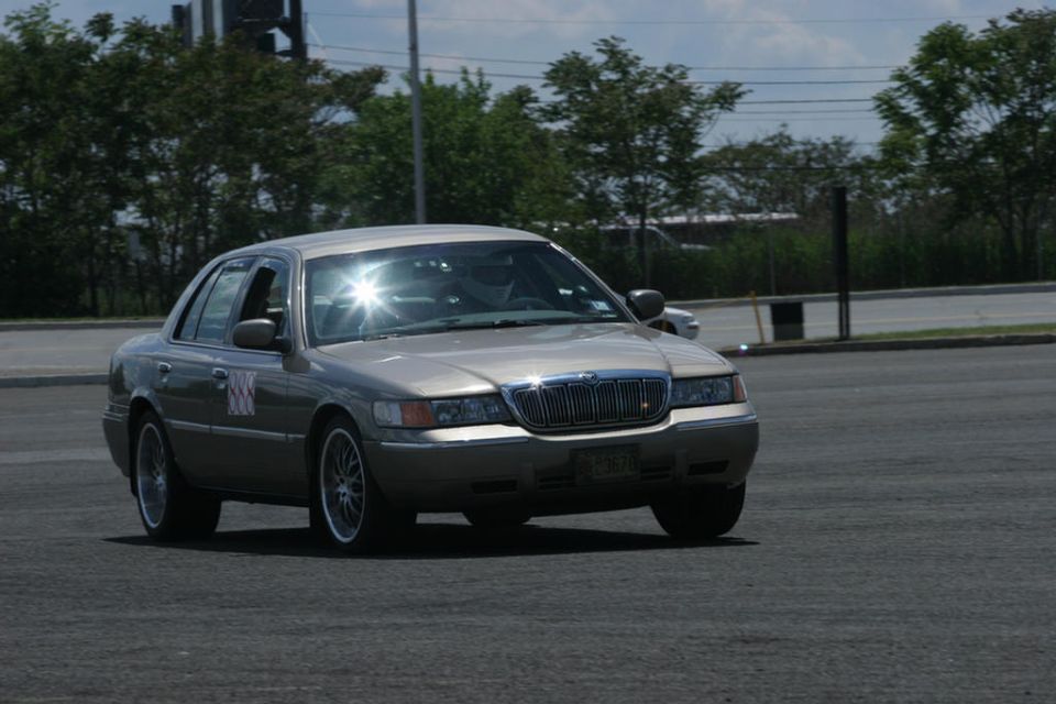 Gold Mercury Grand Marquis sedan cornering on asphalt autocross course