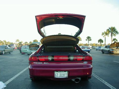 1994 Ford Probe - A red hatchback with its trunk open, parked in a lot with other vehicles. The license plate reads GT 2ENVY.