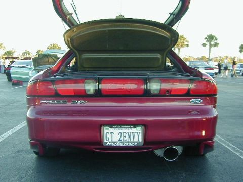 1994 Ford Probe - Rear view of a red 1994 Ford Probe GT, showing the trunk and gullwing doors open, with other vehicles in the background.