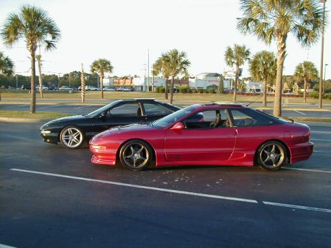1994 Ford Probe - Two Ford Probes, one red and one black, are parked in a lot with palm trees in the background.
