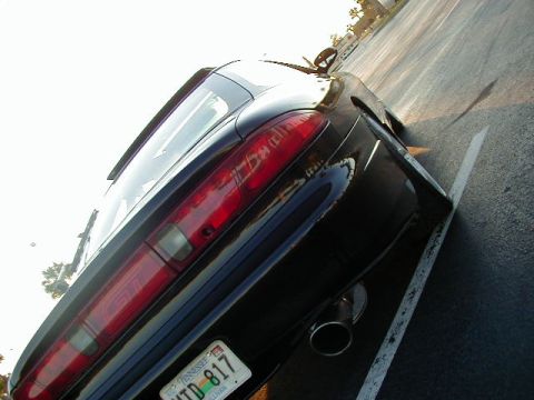 1994 Ford Probe - The rear of a black sports coupe is visible, parked at an angle in a lot with a white line on the asphalt.