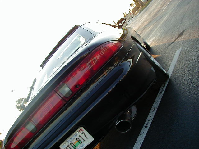 Black sports coupe parked in a lot, rear quarter view. Shows taillight and exhaust pipe