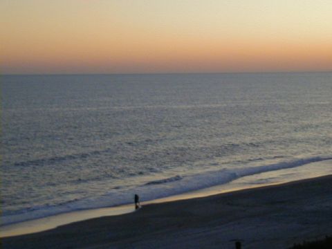 1994 Ford Probe - A lone figure walks along the shore as the sun sets over the ocean, creating a beach scene.