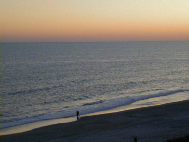 Beach scene with a person walking by the ocean at sunset