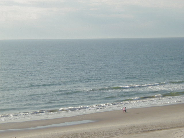 Beach scene with ocean waves and two people walking on the sand. Supermotors.net logo in the corner