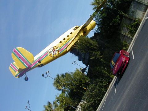1994 Ford Probe - A red coupe is parked on asphalt next to a yellow airplane with colorful stripes and 'Island Charters' written on its side.