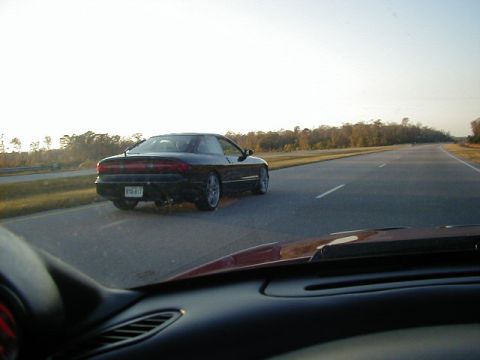 1994 Ford Probe - A black coupe is seen from behind on a highway under a bright sky.