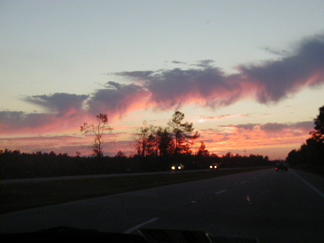 Highway sunset scene with two distant cars and colorful clouds