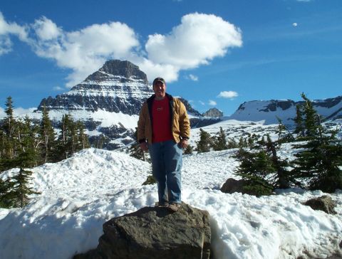 1996 Ford Bronco - A man stands on a rock in a snowy mountain landscape under a bright blue sky with clouds.