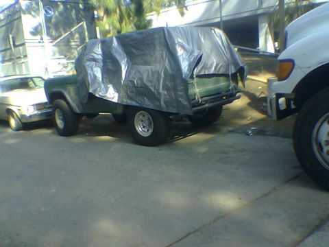 1988 Ford Bronco - A green SUV is mostly covered by a tarp, parked on a street next to other vehicles.