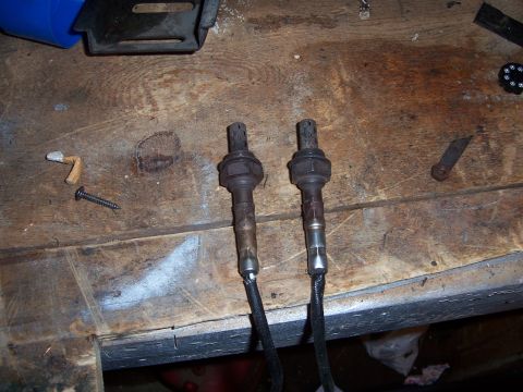 1997 Ford Probe - Two oxygen sensors are laid out on a workbench next to a screw and other small parts.