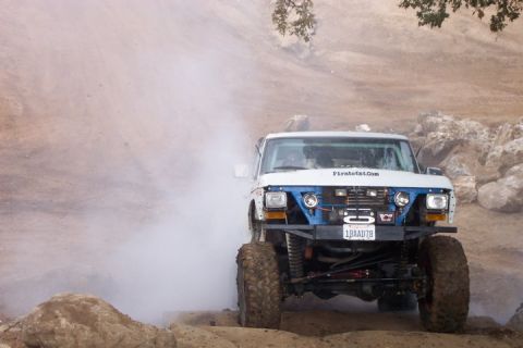 1989 Ford Bronco - This modified truck is navigating a challenging off-road course, generating a cloud of dust.