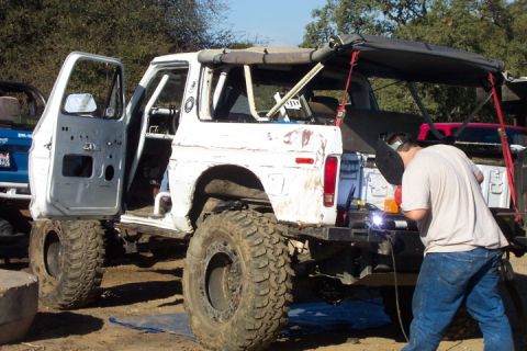1989 Ford Bronco - A man welds the rear bumper of a heavily modified white Ford Bronco, with another vehicle visible behind it.