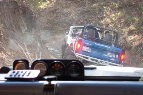 1989 Ford Bronco - A blue Ford Bronco navigates a rough dirt road, with another vehicle visible ahead.