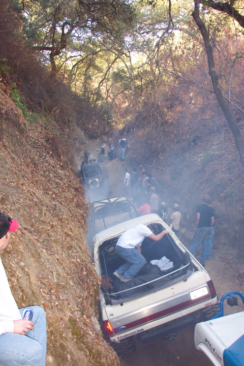 1989 Ford Bronco - Multiple off-road vehicles navigate a steep, dusty trail with onlookers present.