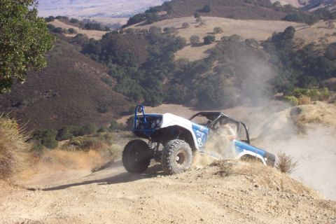 1989 Ford Bronco - An off-road buggy navigates a dusty trail in a hilly, arid landscape.