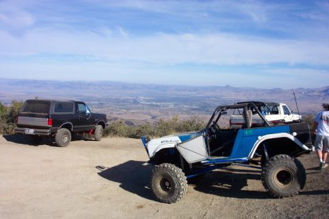 1989 Ford Bronco - Two off-road vehicles are parked on a hill overlooking a valley town.