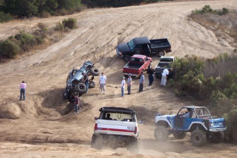 1989 Ford Bronco - Multiple off-road vehicles navigate a challenging dirt terrain, with one vehicle tipped on its side.