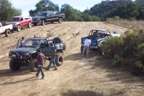 1989 Ford Bronco - A blue Ford Bronco with a roll cage is being pulled by a rope on a dirt hill, with other vehicles present.