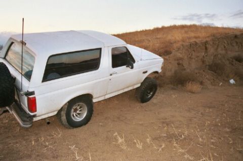1993 Ford Bronco - A white Ford Bronco is parked on a dirt embankment under a cloudy sky.