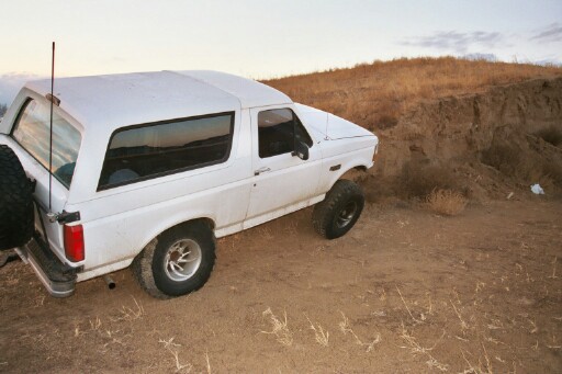 White Ford Bronco parked on dirt with a spare tire mounted on the rear