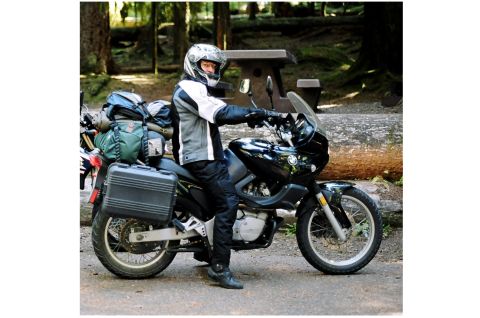 1976 Ford F-150 - A rider sits on a black motorcycle equipped with saddlebags and packed luggage, parked outdoors.