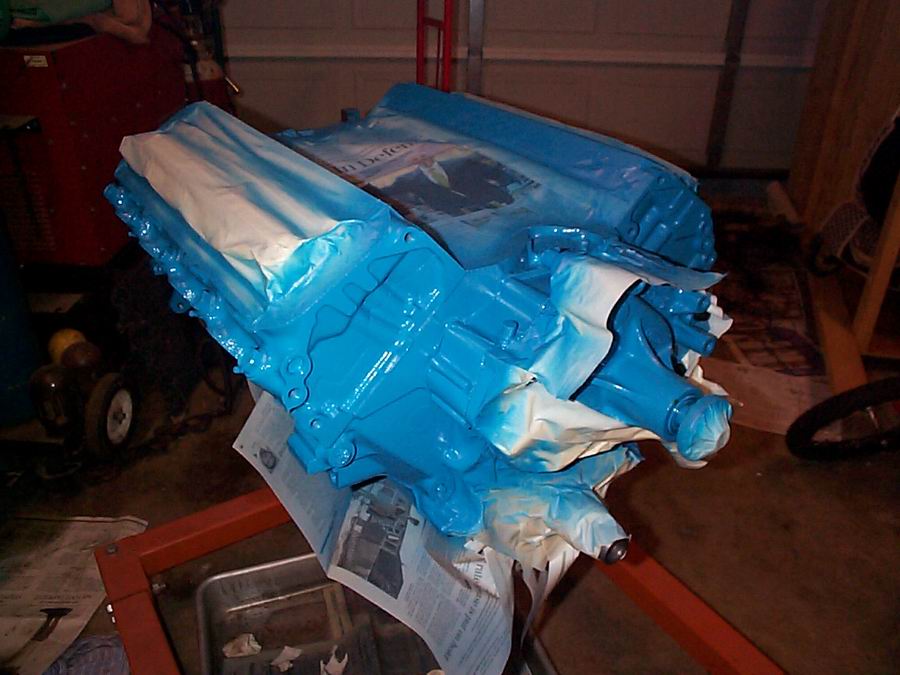Engine block covered in blue paint and masking paper, sitting on an engine stand