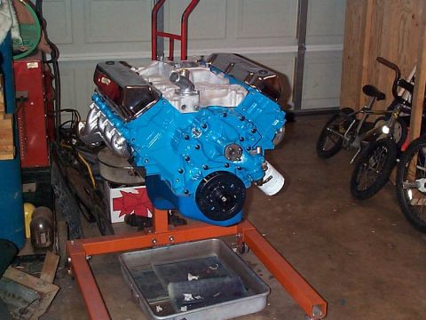 1979 Ford Bronco - A freshly rebuilt V8 engine, painted bright blue, sits on an orange engine stand in a garage setting.
