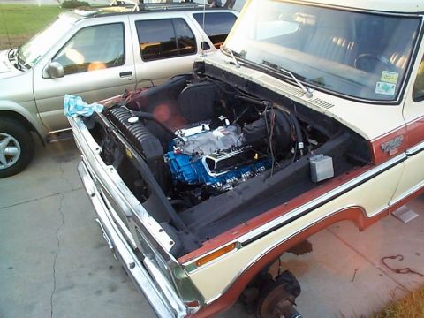 1979 Ford Bronco - A 1979 Ford Bronco's engine bay is visible, with a blue engine and a second vehicle parked nearby.