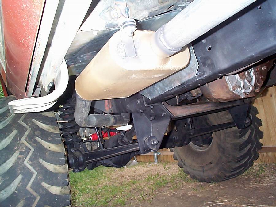 Underside of a vehicle showing exhaust pipe, muffler, suspension, and large tire