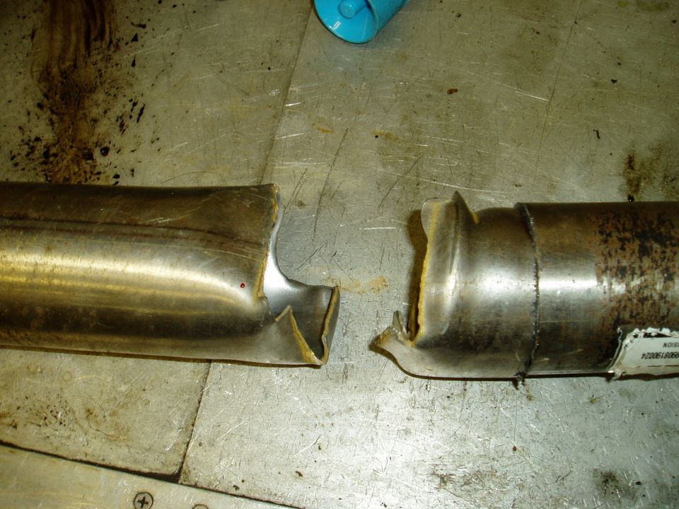 Two cut sections of a metal driveshaft tube lying on a scratched workbench