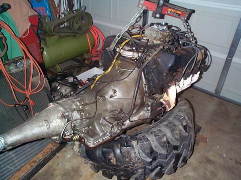 1979 Ford Bronco - Engine and transmission assembly, likely removed from a vehicle, is suspended by a hoist and supported by tires.