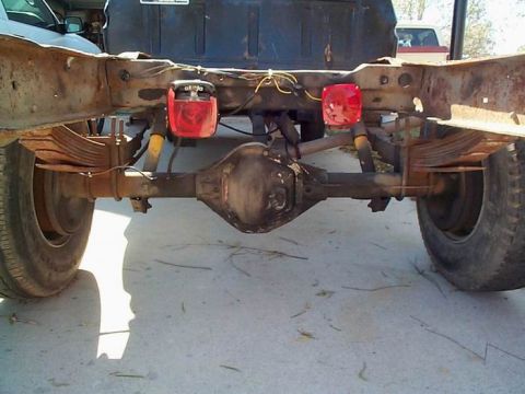 1979 Ford Bronco - Close-up of a truck's rear axle and suspension components, with another vehicle in the background.