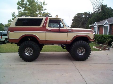1979 Ford Bronco - Side profile of a lifted two-tone Ford Bronco, cream body with red-brown roof, lower panels, and fender flares, riding tall mud-terrain tir…