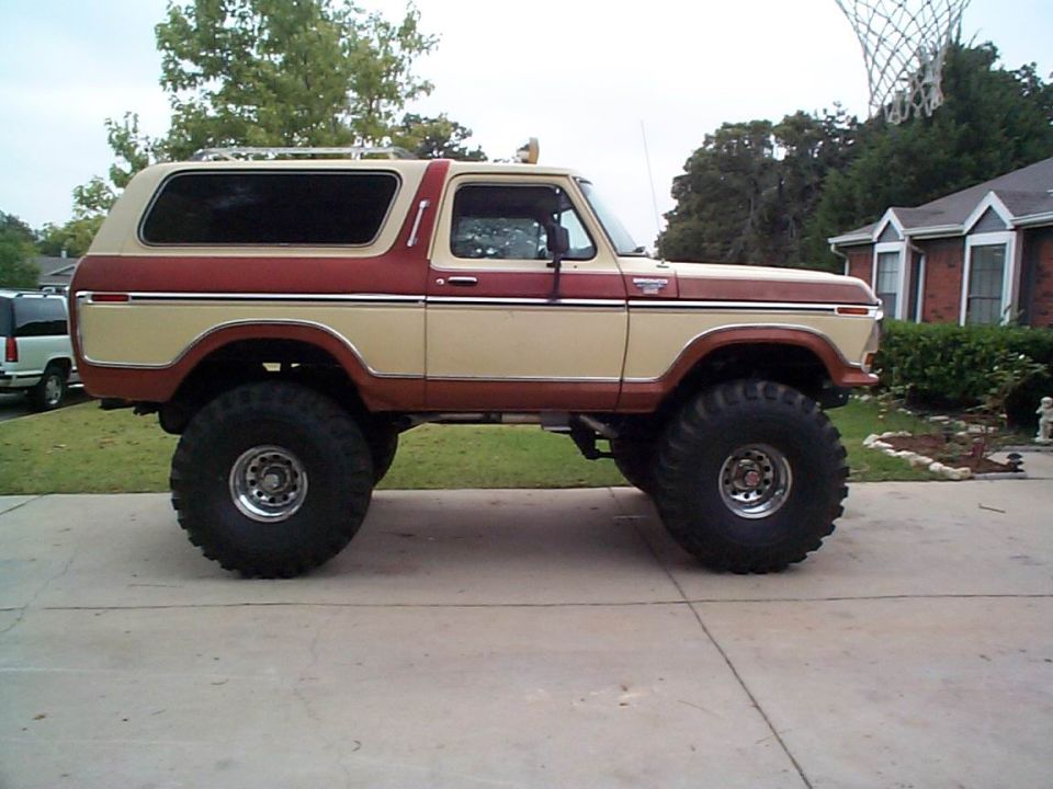 Lifted two-tone tan and red-brown Ford Bronco on tall mud tires, side profile in a driveway