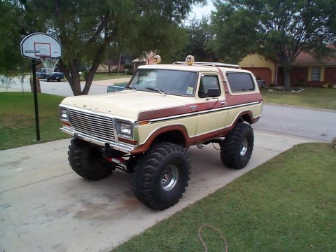 1979 Ford Bronco - A tan and brown two-tone lifted Ford Bronco full-size SUV shown from the front three-quarter angle, sitting on large off-road mud tires wit…