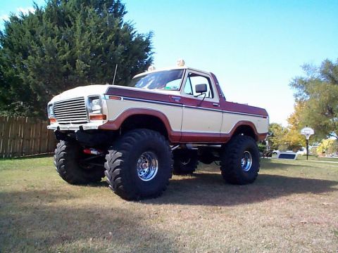 1979 Ford Bronco - Lifted two-tone tan and burgundy full-size Ford Bronco with the rear top removed, photographed from a low 3/4-front angle on a grassy lawn…