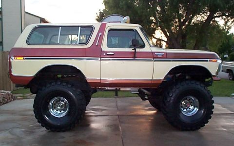 1979 Ford Bronco - Side profile of a heavily lifted two-tone red and cream full-size Ford Bronco with a removable hardtop, parked on a concrete driveway. Huge…