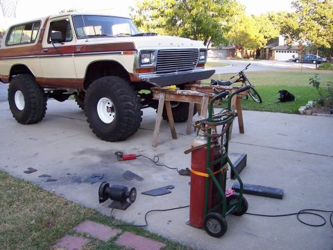 1979 Ford Bronco - A lifted Ford Bronco is parked on sawhorses, with tools and welding equipment set up for custom bumper work.