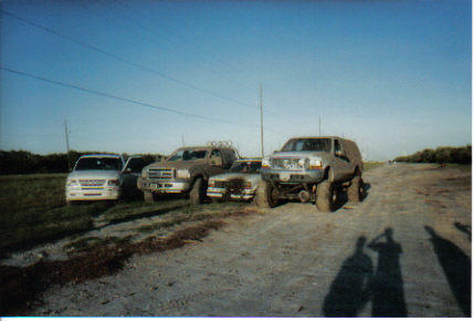 2000 Ford Excursion - Several vehicles are parked on a dirt road under a clear blue sky.