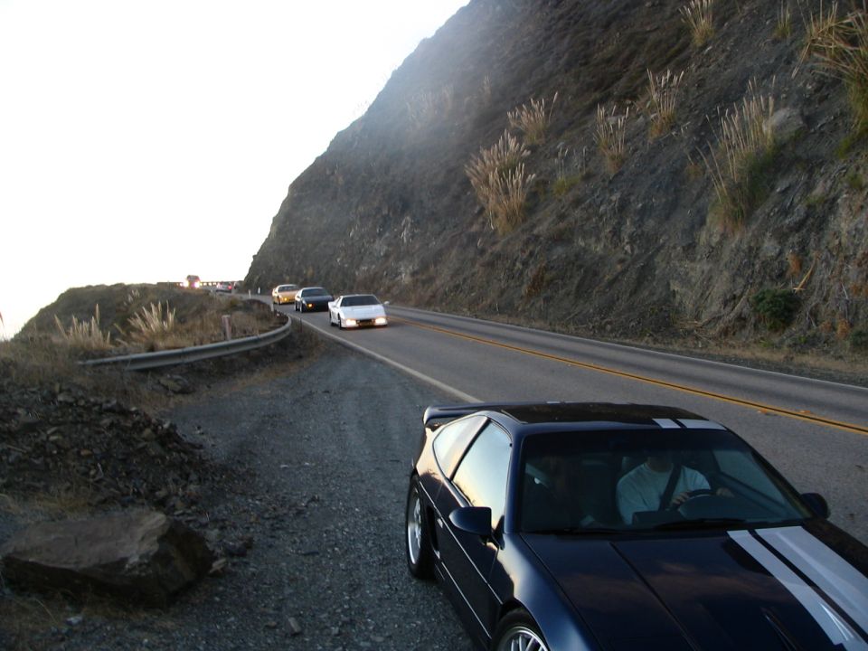 Dark blue 1986 Pontiac Fiero with white stripes on a coastal road