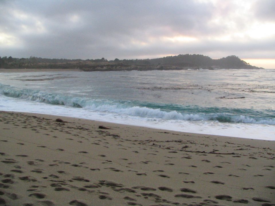 Beach with waves crashing and footprints in the sand under a cloudy sky