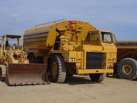 1966 International School Bus - A yellow Caterpillar water truck is parked outdoors with other heavy machinery.