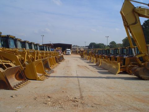 1966 International School Bus - Numerous yellow construction vehicles are lined up in an outdoor lot.