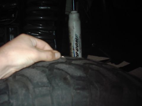 1978 Ford Bronco - A hand removes a nail from a tire, with a shock absorber in the background.