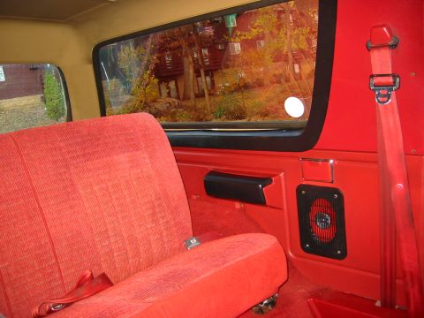 1990 Ford Bronco - Interior view of a vehicle showing red seats and a window looking out onto a wooded area with houses.