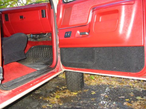 1990 Ford Bronco - The red interior of a vehicle is shown, with a focus on the door panel and dashboard area.