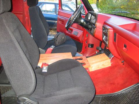 1990 Ford Bronco - The interior of a red truck shows black seats and a wooden console, with another vehicle visible outside.