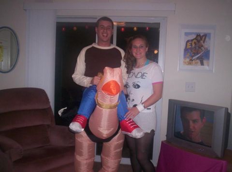 2001 Ford Taurus - Two people in costumes pose for a photo indoors, with a television displaying a man's face in the background.